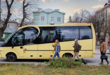 Alquiler de autocares crece como solución eficiente para la movilidad grupal A yellow passenger bus on a city street with three pedestrians walking nearby, each carrying a drink or luggage as they pass.