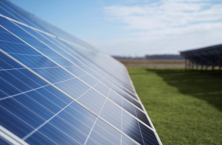 Solar panels angled across a grassy field under a clear blue sky, harvesting sunlight for renewable energy.