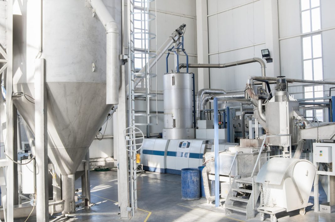 Industrial processing plant interior with tall stainless steel tanks, connected pipes, and control panels.