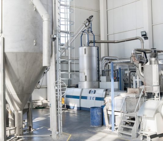 Equipos periféricos para plástico: una producción más sostenible Industrial processing plant interior with tall stainless steel tanks, connected pipes, and control panels.