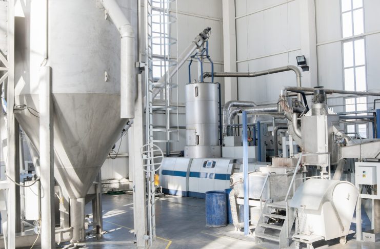 Industrial processing plant interior with tall stainless steel tanks, connected pipes, and control panels.
