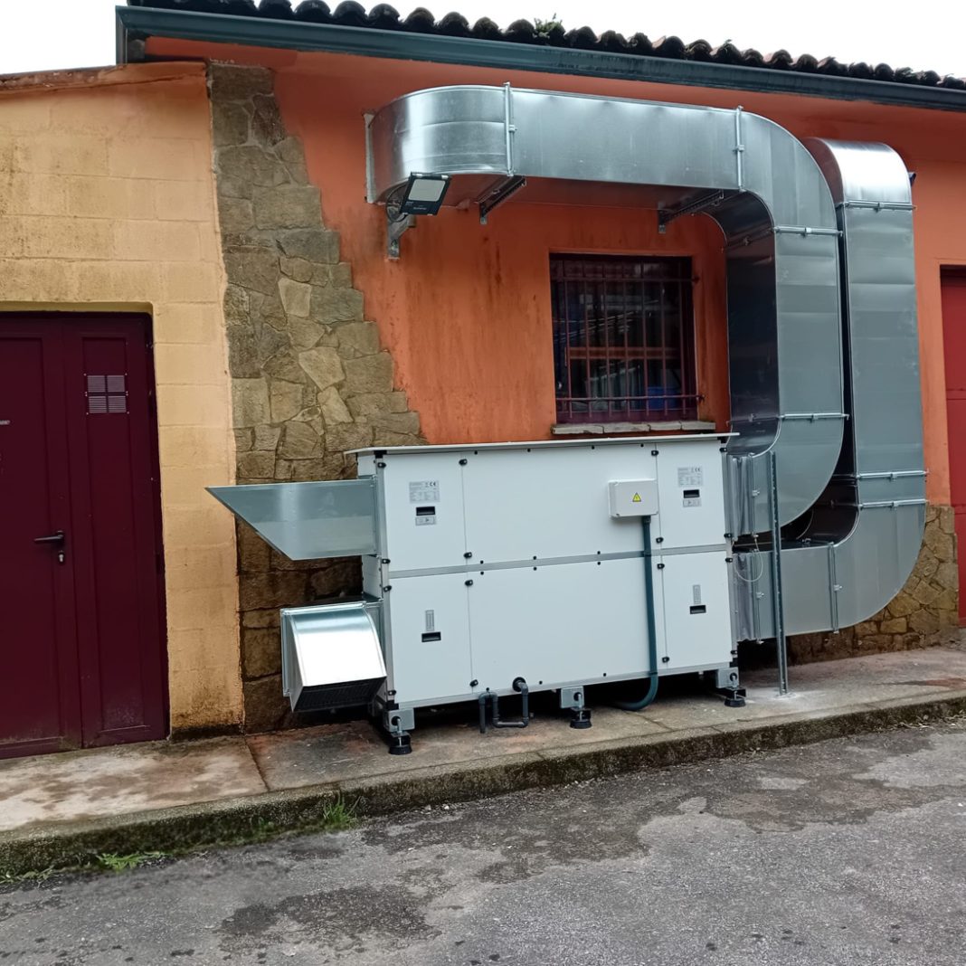 La discrepancia entre el INSST y el CSN crea dudas en las obras de corrección de radón Outdoor industrial HVAC system: large galvanized ducts connected to a white air handling unit against an orange wall with a barred window and stone column nearby.