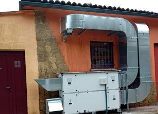 La discrepancia entre el INSST y el CSN crea dudas en las obras de corrección de radón Outdoor industrial HVAC system: large galvanized ducts connected to a white air handling unit against an orange wall with a barred window and stone column nearby.