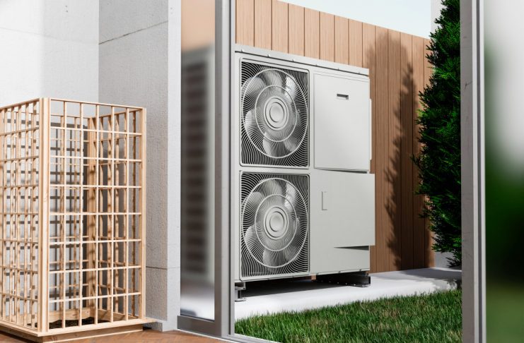 Empresas especializadas acercan soluciones de climatización para proyectos cada vez más eficientes - Outdoor HVAC condenser unit with two large fans mounted inside a glass enclosure beside a wooden privacy screen, with grass nearby.