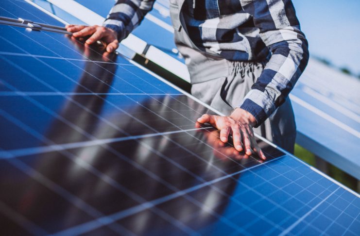 Person in a plaid shirt inspects and touches solar panels in a sunny outdoor installation