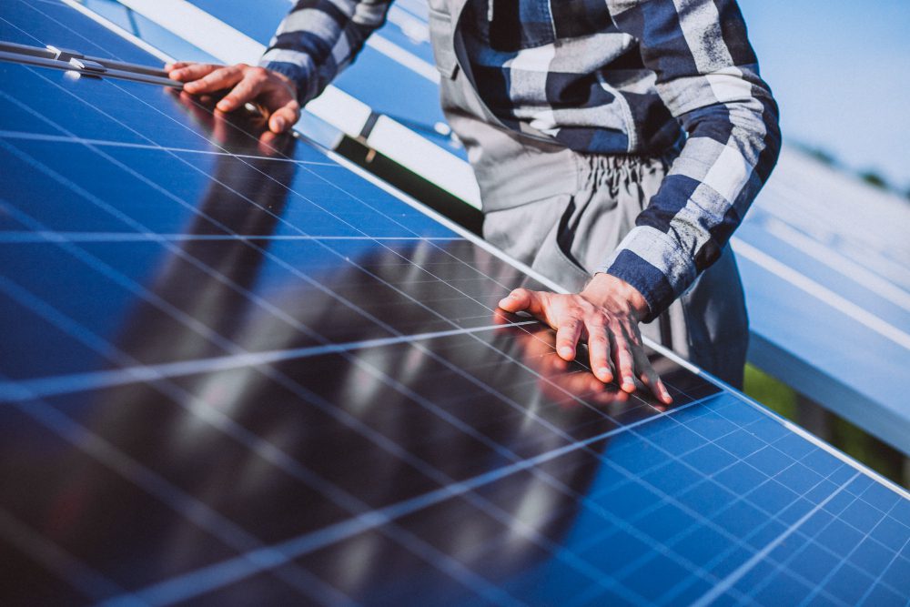 Person in a plaid shirt inspects and touches solar panels in a sunny outdoor installation