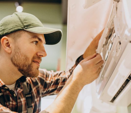 Una instalación profesional de aire acondicionado mejora confort y eficiencia Man in a green cap and plaid shirt adjusting a control panel on a large machine in a workshop setting