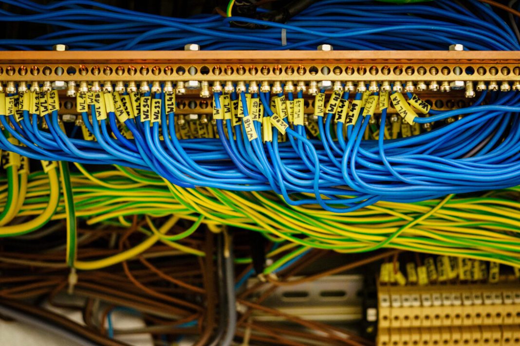 Del cobre a los cables inteligentes: así está cambiando la electricidad Close-up of a network patch panel with blue and yellow Ethernet cables plugged into the ports, cables labeled and tangled in a data rack.