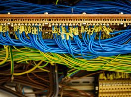 Close-up of a network patch panel with blue and yellow Ethernet cables plugged into the ports, cables labeled and tangled in a data rack.